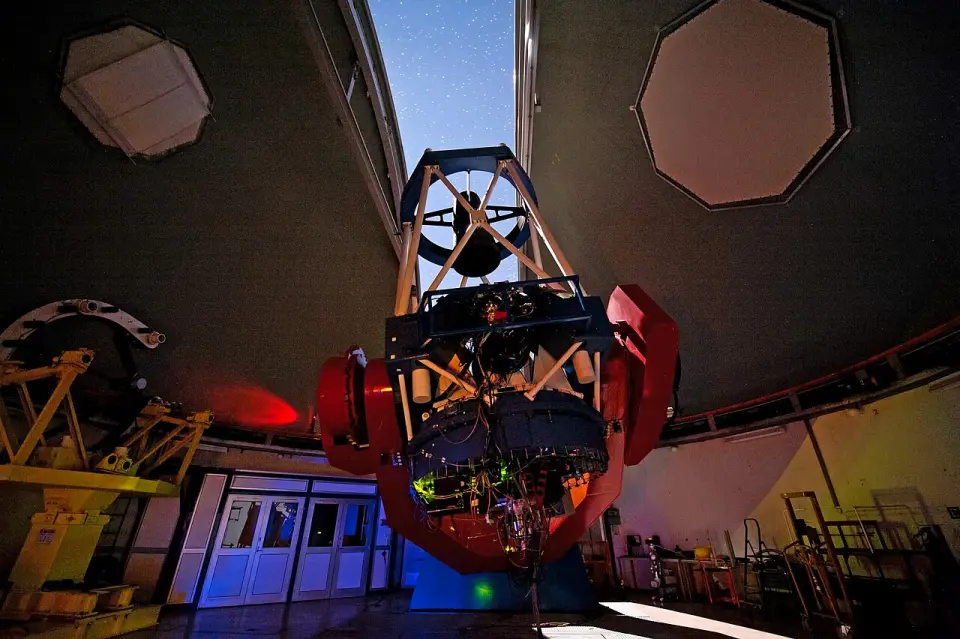 A large telescope inside an open observatory dome at dusk