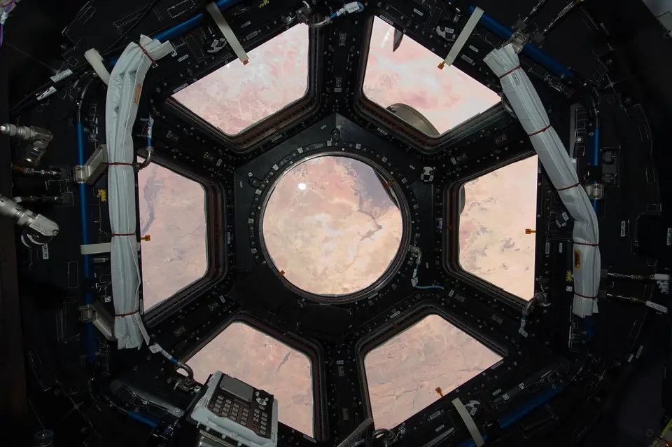 The seven windows of a space station's cupola looking down on a desert