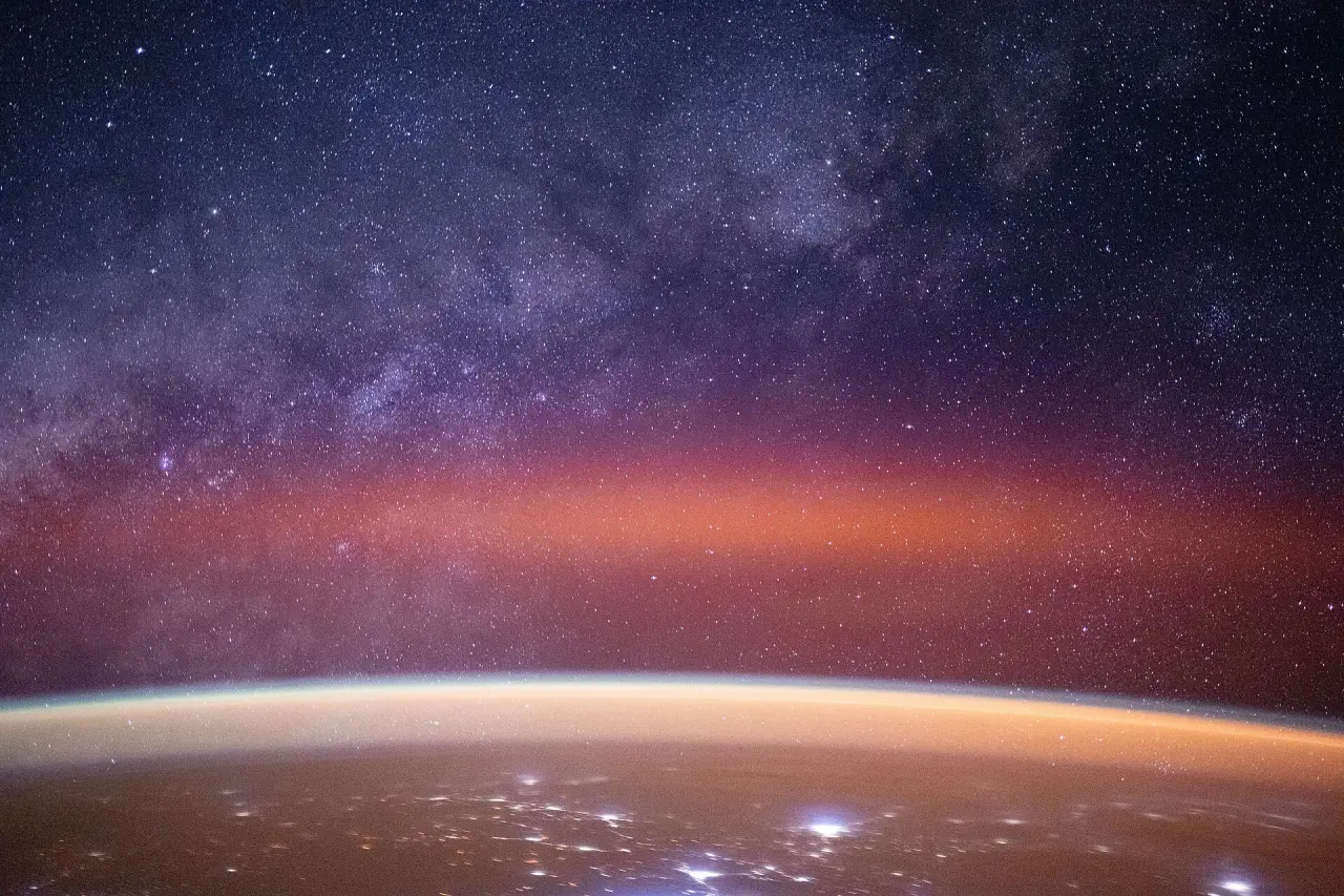 The Milky Way above a band of orange airglow on Earth's horizon, seen from orbit