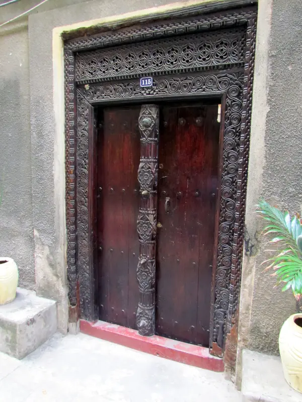 A tall dark teak door with a carved central post and brass studs in a lime-plastered wall