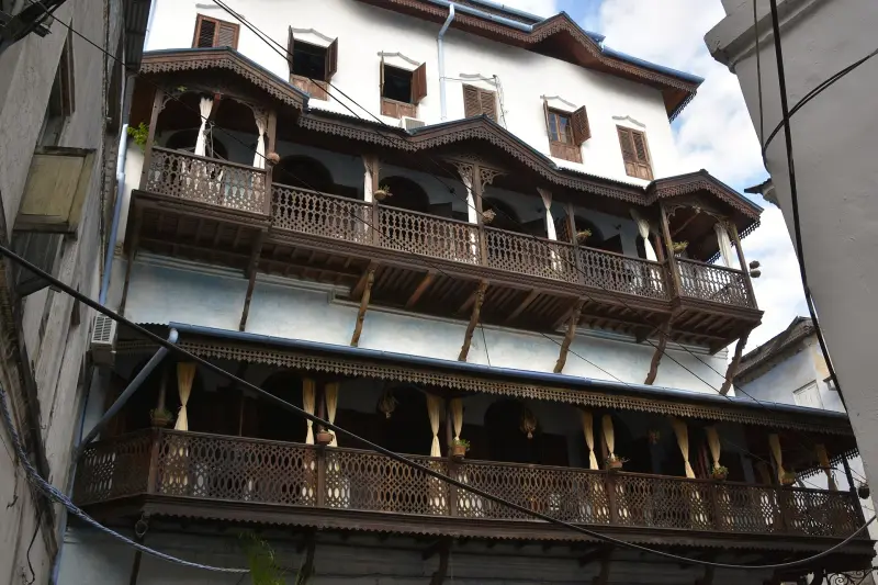 A whitewashed Stone Town house with two storeys of carved dark-wood balconies over a narrow lane