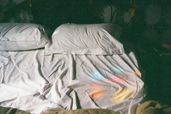 Morning light through a coloured-glass fanlight falling across white bed linen
