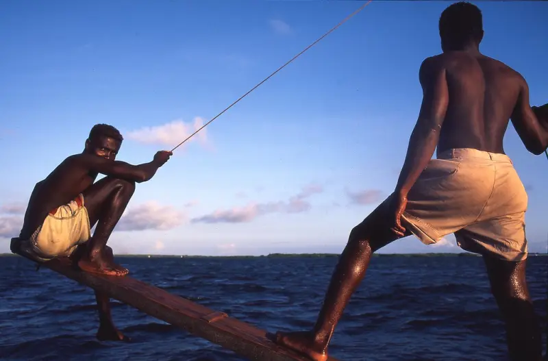 Two dhow crewmen balancing on the boom above open water off Lamu