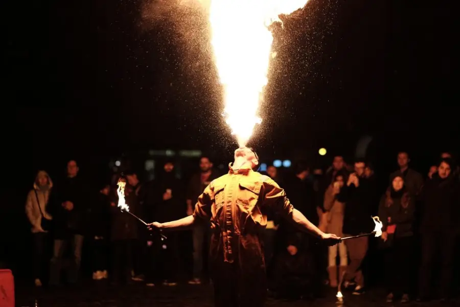 A performer breathing a column of fire at night in front of a crowd