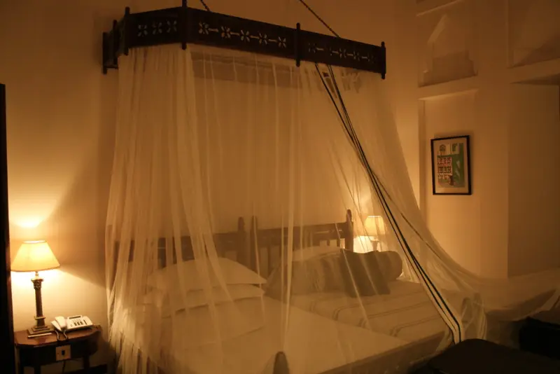 A carved four-poster bed under a white mosquito net in a warmly lit room