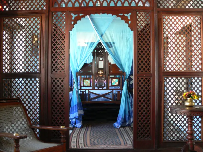 Carved wooden lattice screens framing a canopy bed hung with turquoise drapes