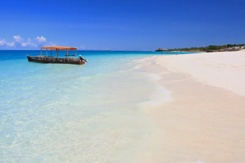 A wooden boat moored in clear turquoise water off a white beach