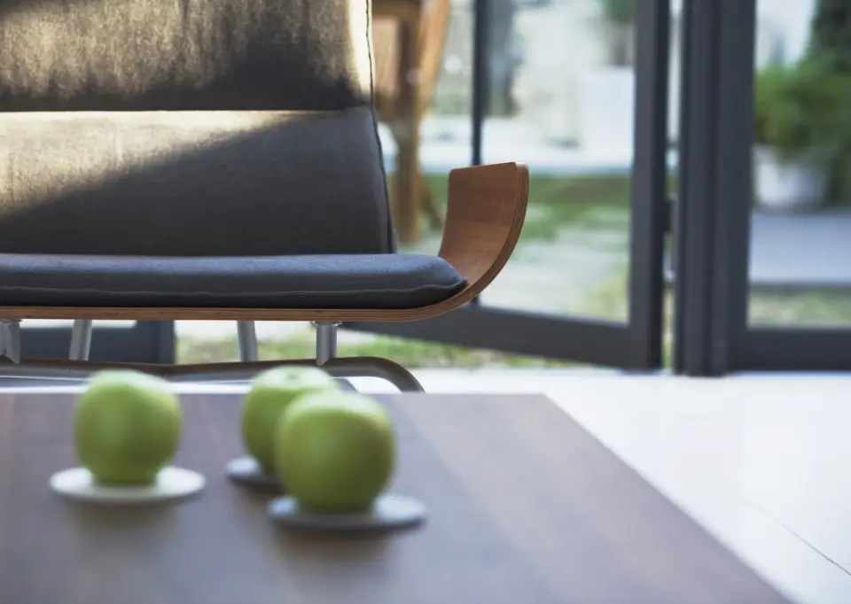 Green apples on a walnut table beside a dark armchair