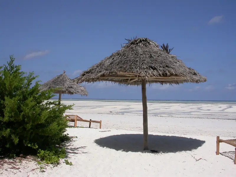 A thatched beach umbrella on white sand under a blue sky